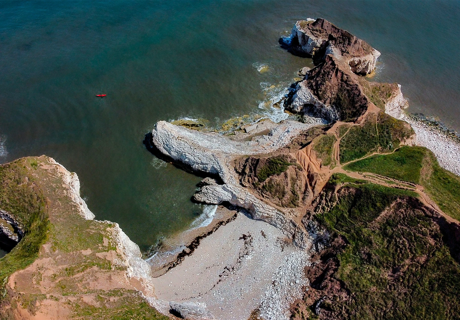 A kayaker paddles past white chalk headlands and a small cove seen from above