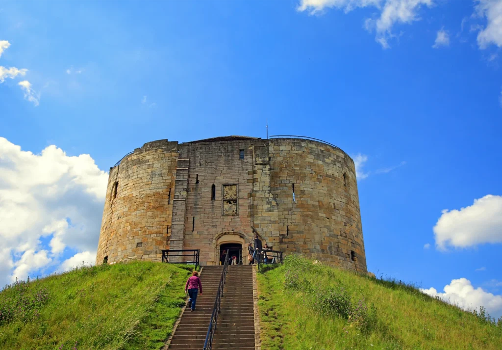 Visitors climb a long flight of steps to a round medieval stone tower under blue sky