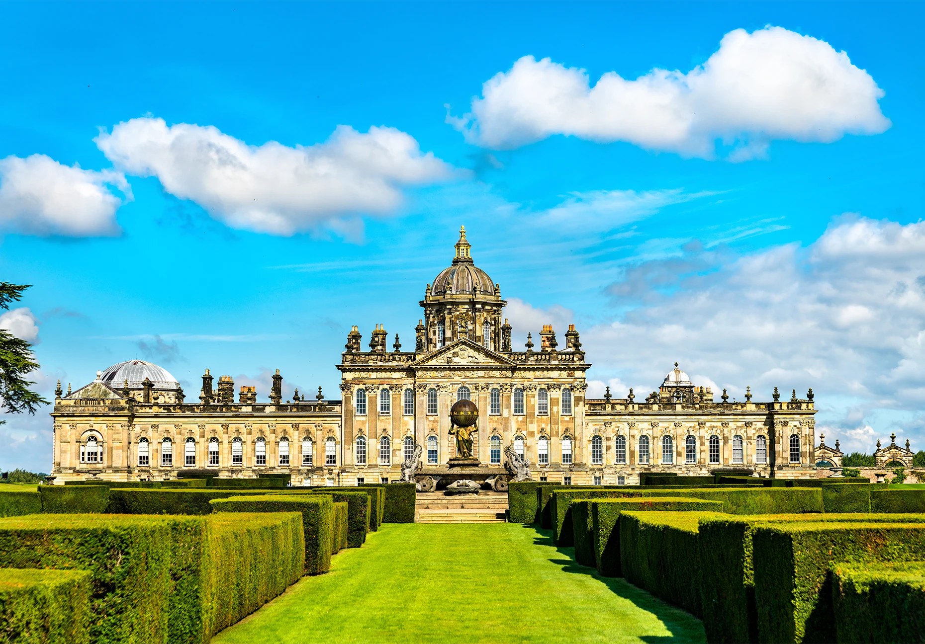 The domed baroque facade of Castle Howard rises beyond clipped hedges and a grass walk