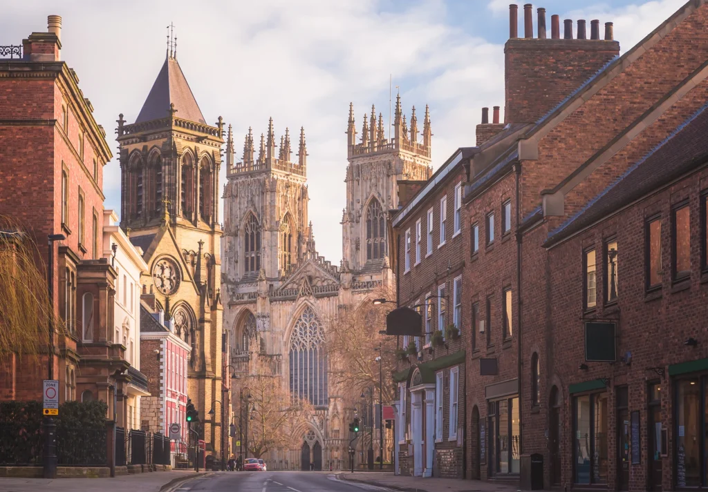 The west front of York Minster rises at the end of a quiet brick-lined street at dawn