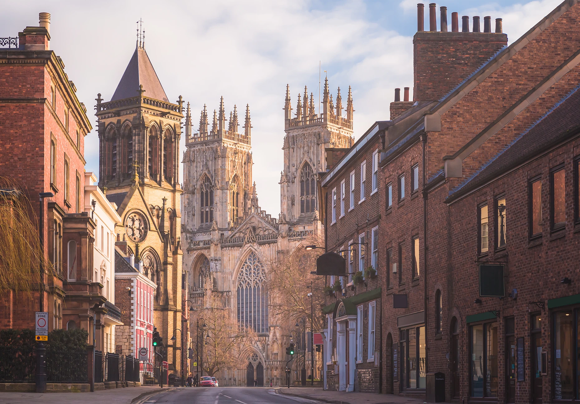 The west front of York Minster rises at the end of a quiet brick-lined street at dawn