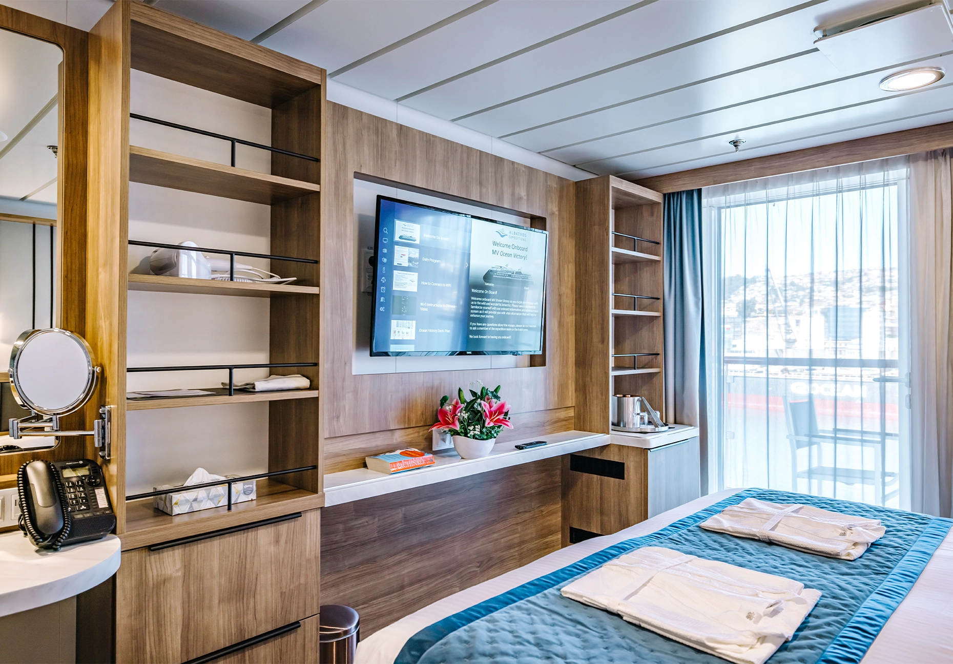 Cabin with wood paneling, teal bedspread, folded robes, wall television, and balcony doors