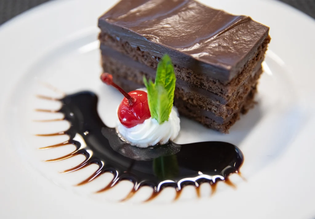 Layered chocolate cake with cherry, cream, and mint beside a dark sauce swirl