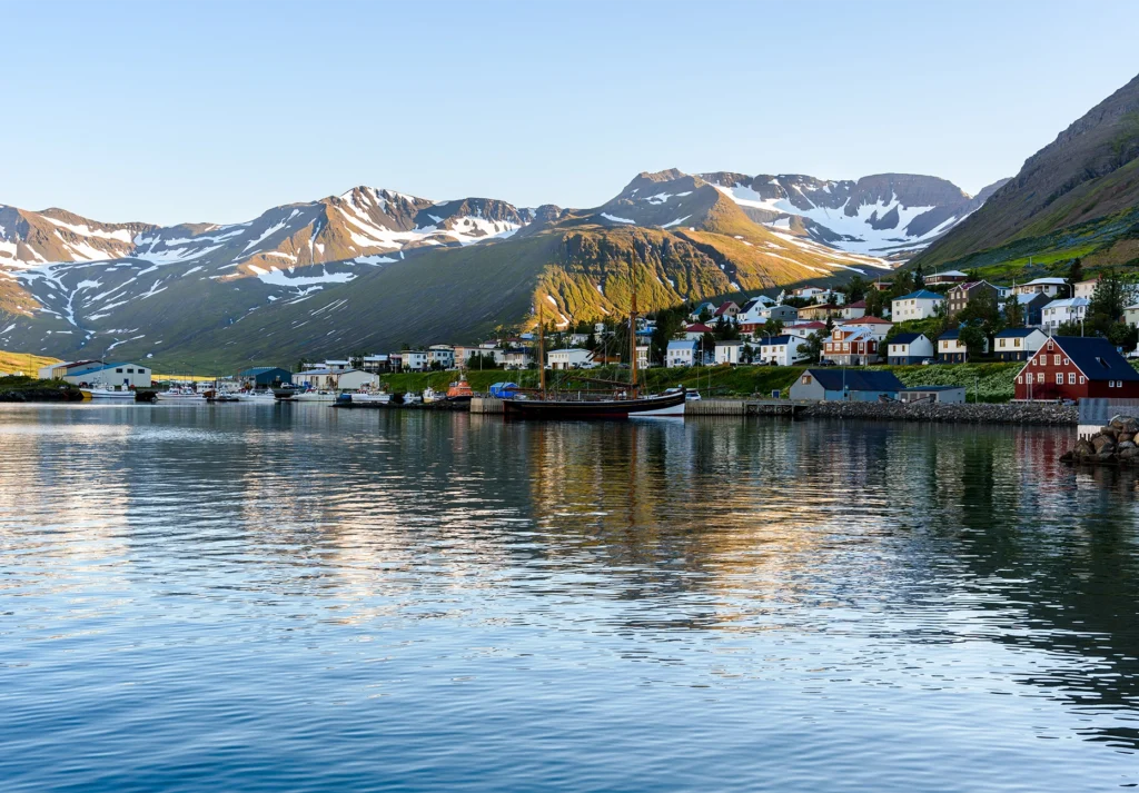 Colorful houses and moored boats along a calm fjord below snow-streaked mountains