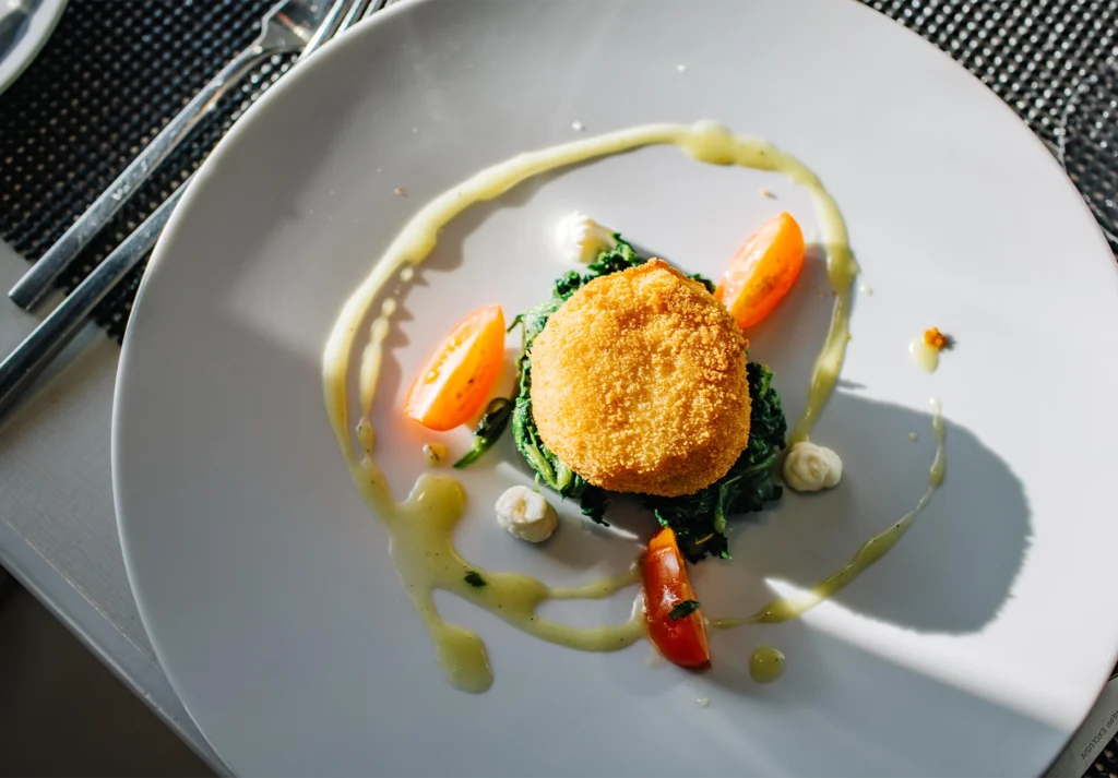 Golden breaded croquette on wilted greens with tomato wedges and drizzled sauce
