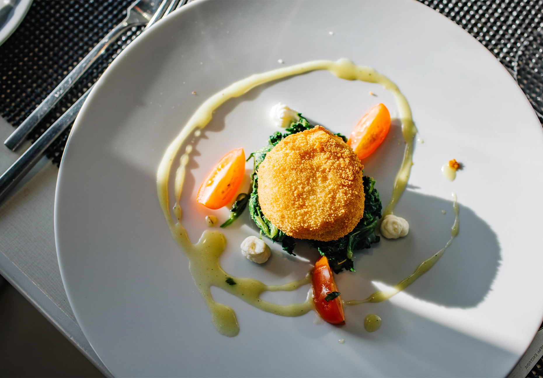Golden breaded croquette on wilted greens with tomato wedges and drizzled sauce