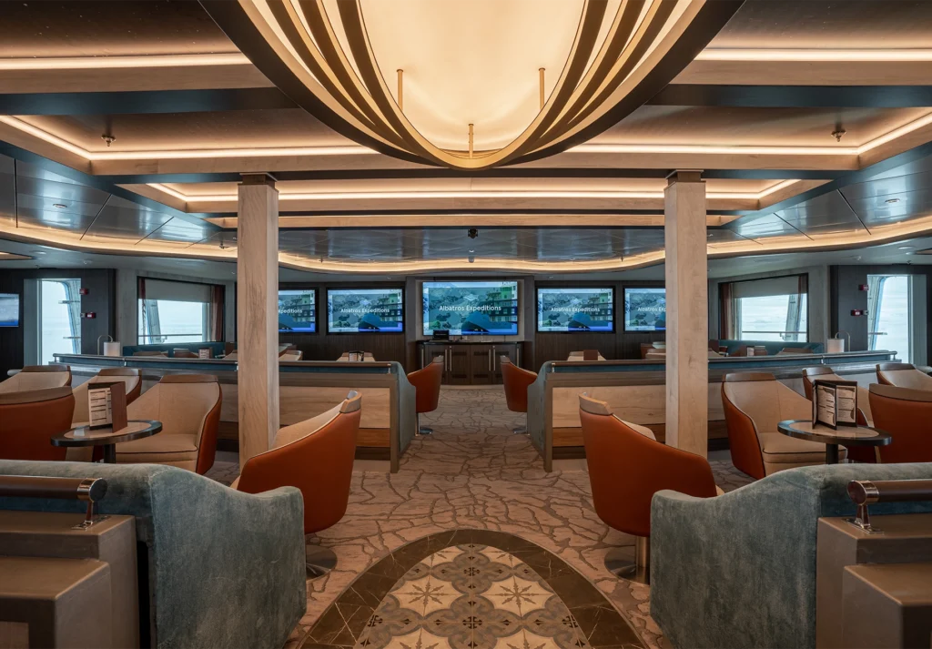 Tiered seating with orange and blue chairs facing a bank of presentation screens