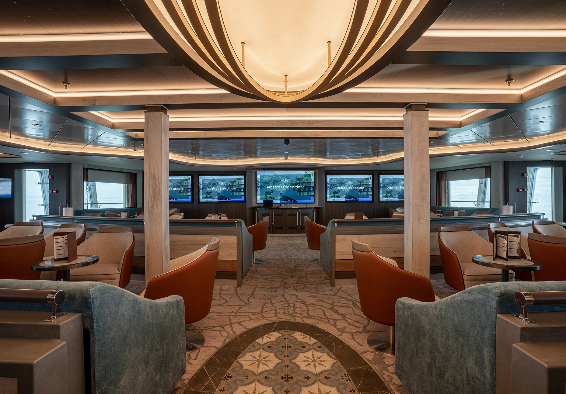 Tiered seating with orange and blue chairs facing a bank of presentation screens