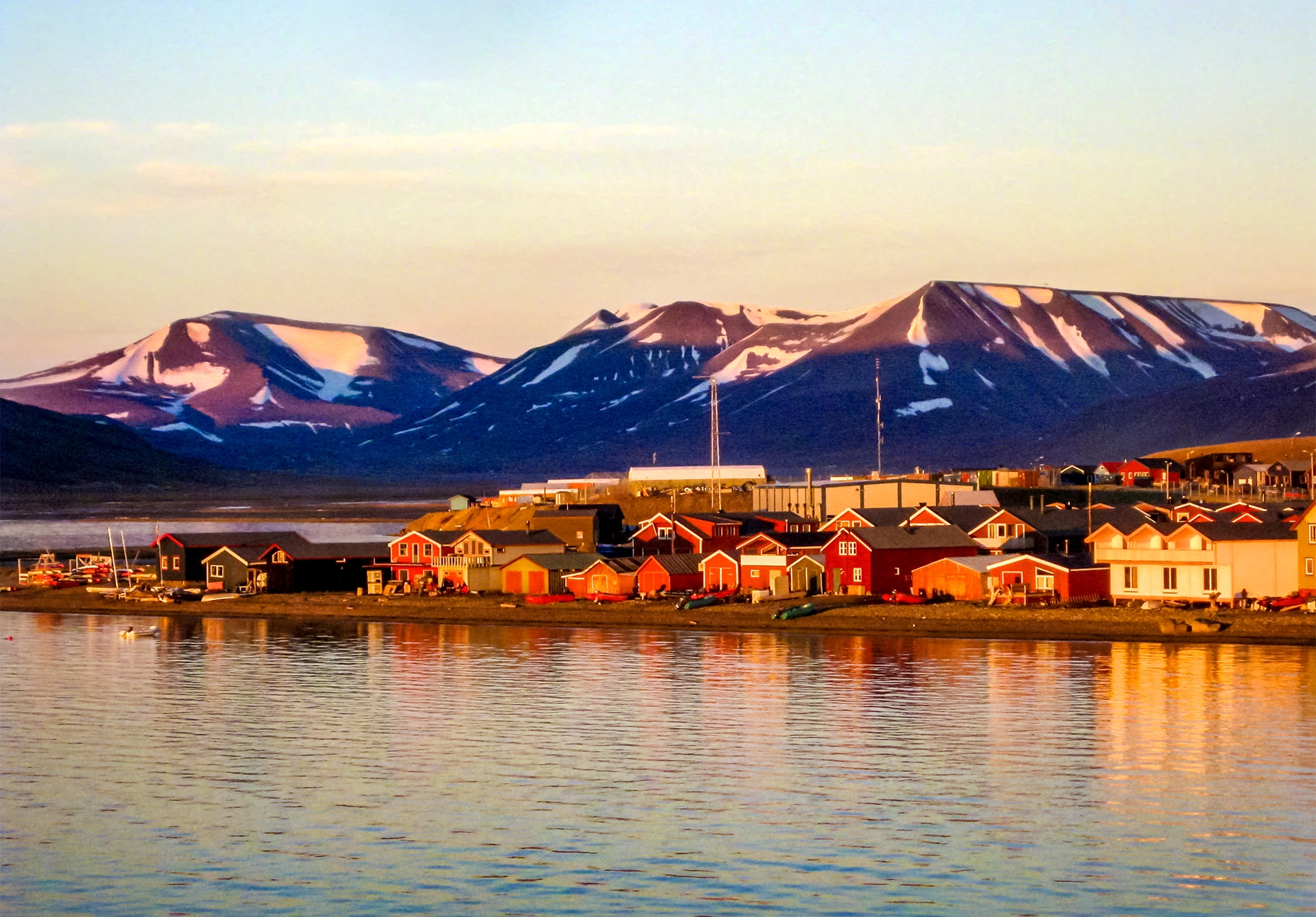Red and white timber houses along the shore glowing gold beneath snow-streaked mountains