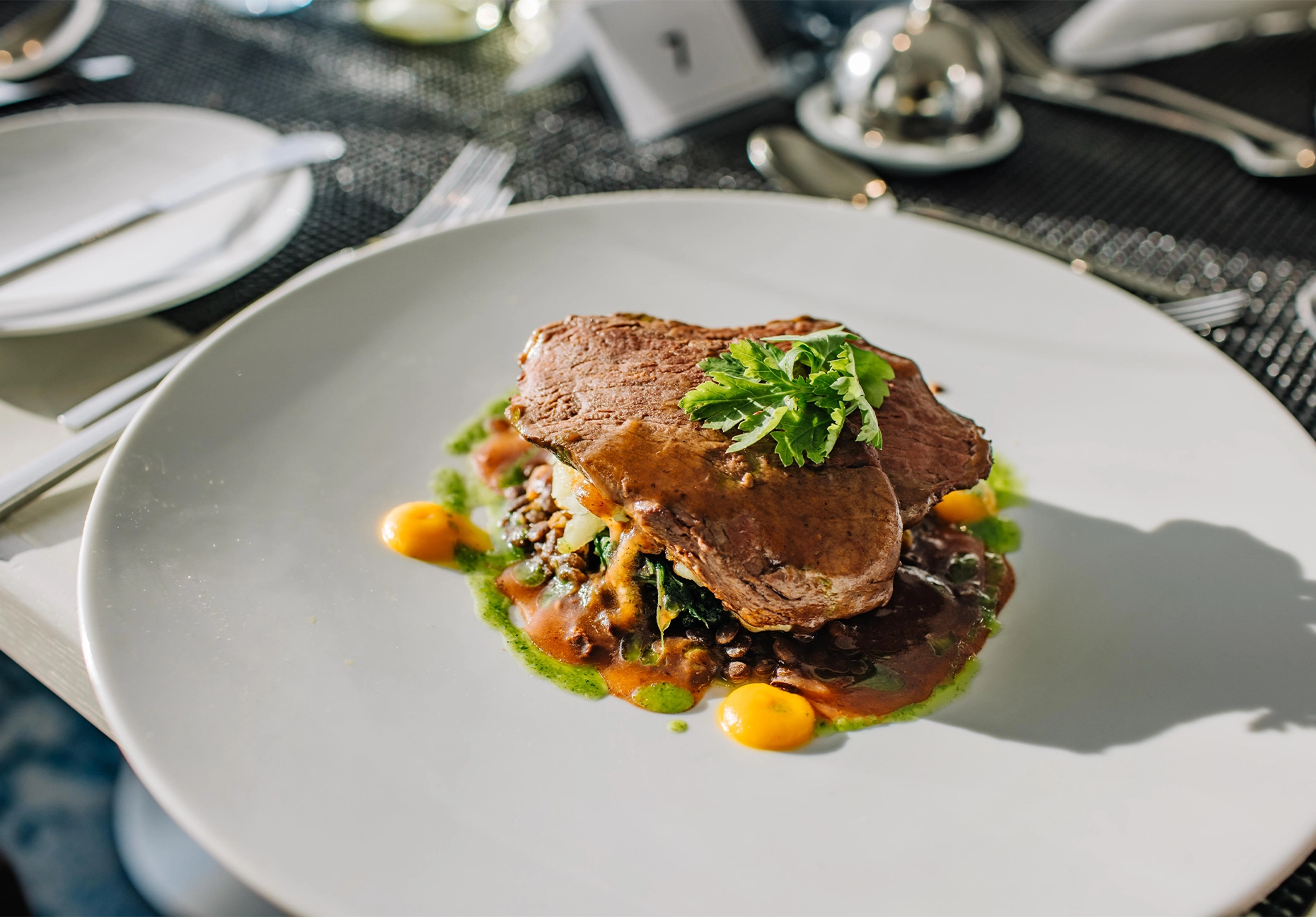 Sliced beef on lentils and greens with herb garnish and dots of orange puree