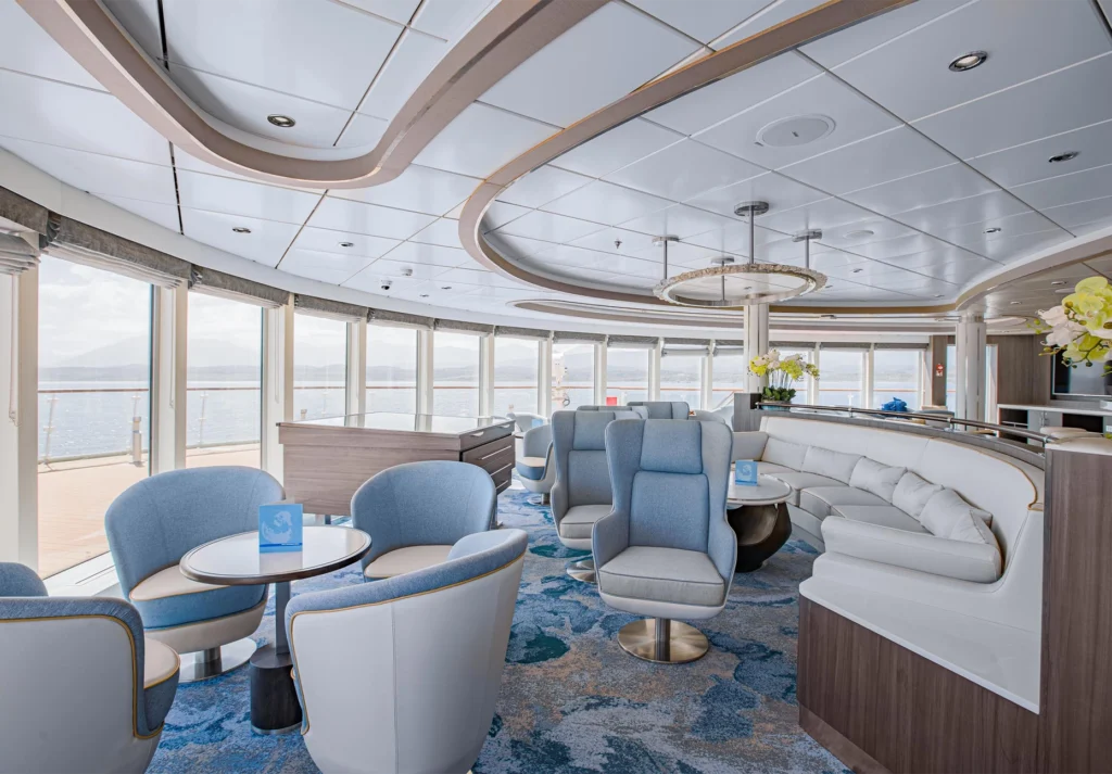 Armchairs and curved sofa seating beside floor-to-ceiling windows overlooking the sea
