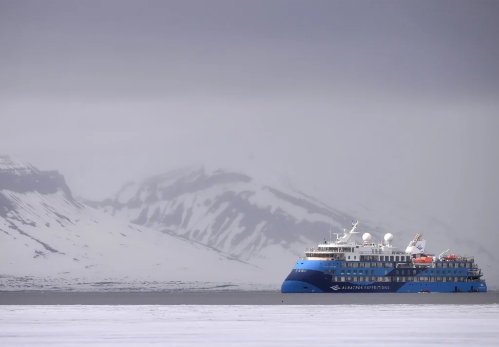 Blue Albatros Expeditions ship on gray water below a fog-shrouded snowy mountain