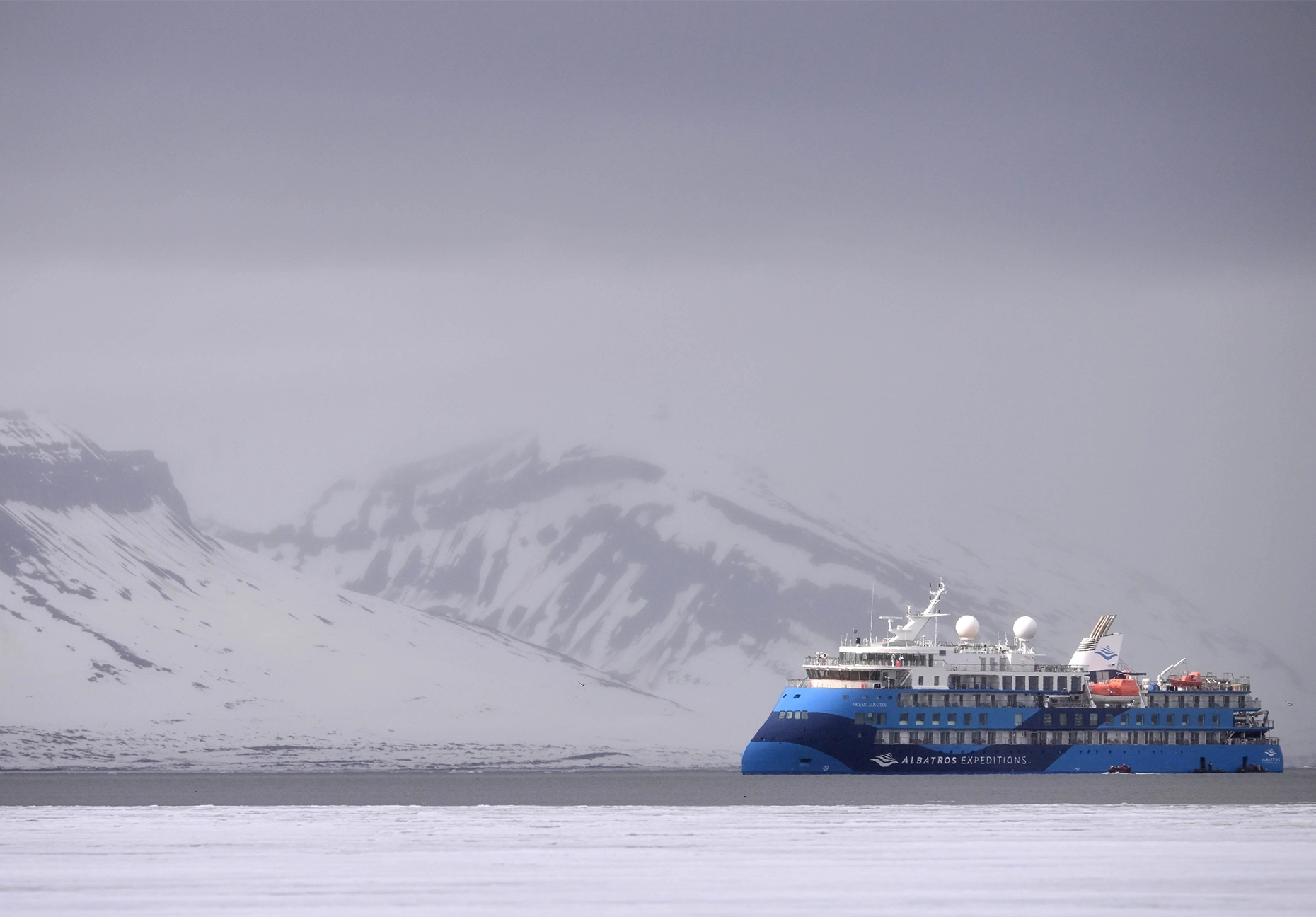 Blue Albatros Expeditions ship on gray water below a fog-shrouded snowy mountain