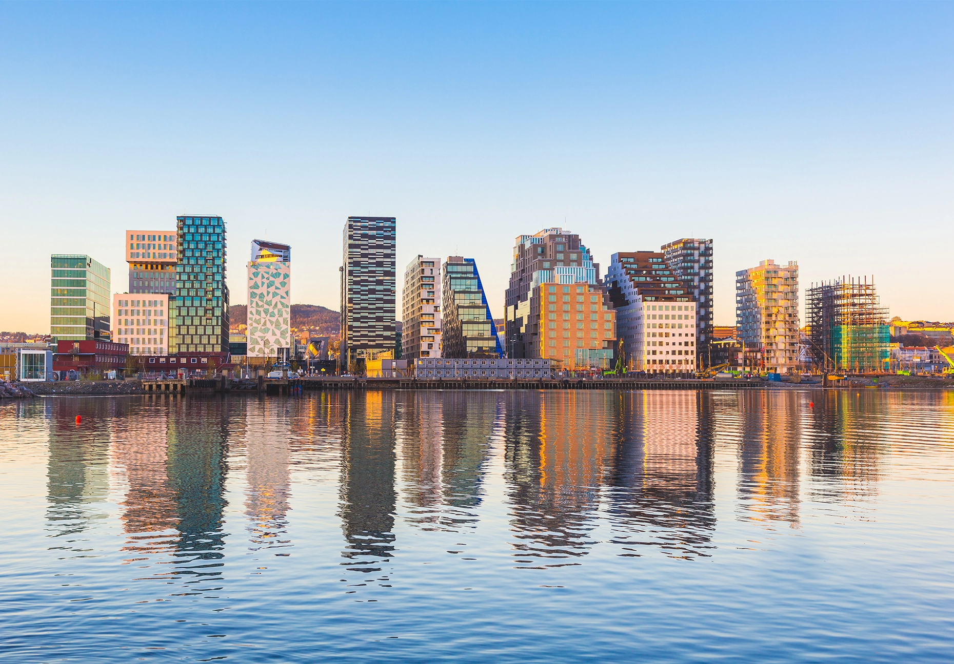Row of modern high-rise buildings mirrored in calm harbor water under a clear sky