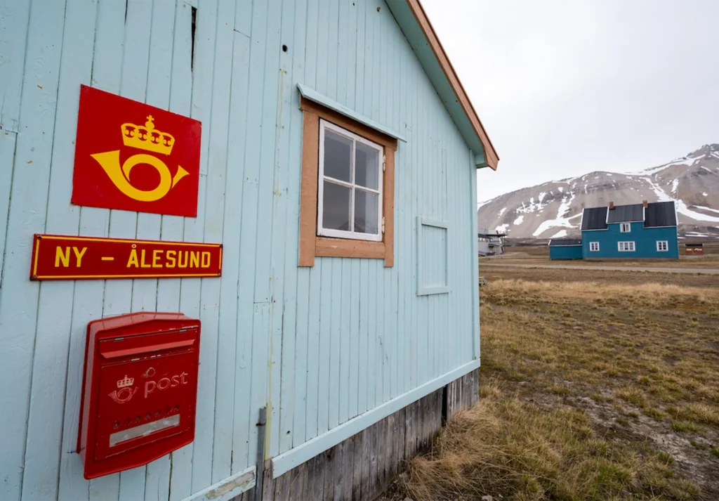 Red Norwegian post sign and mailbox on a pale blue timber wall with mountains behind