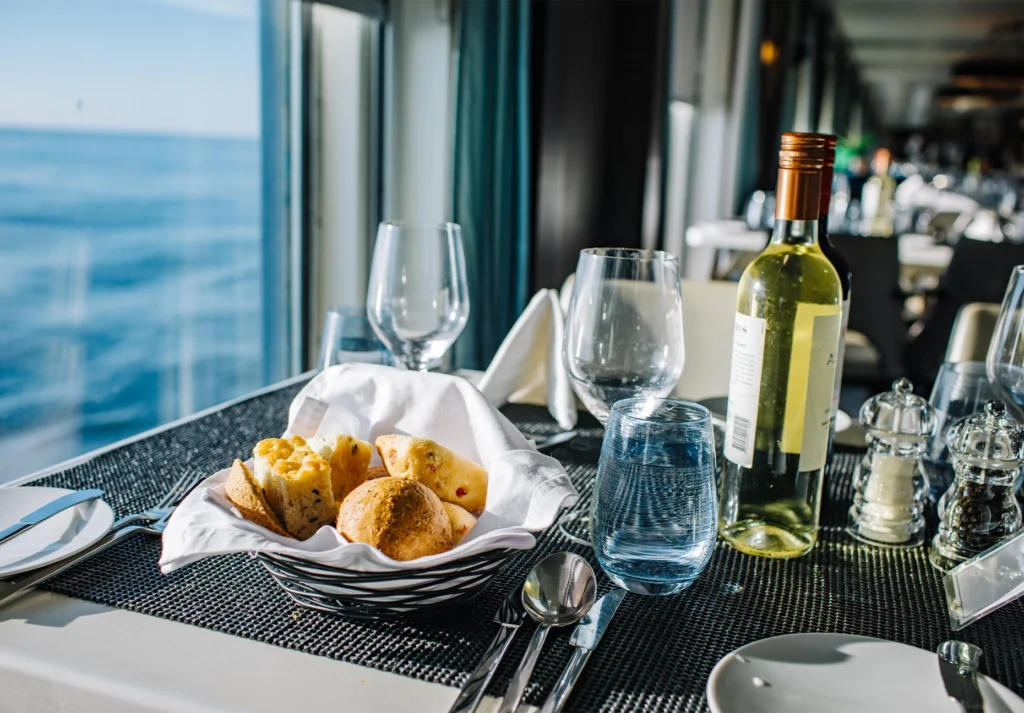 Bread basket, wine bottle, and glassware on a set table beside a sea-facing windowBread basket, wine bottle, and glassware on a set table beside a sea-facing window