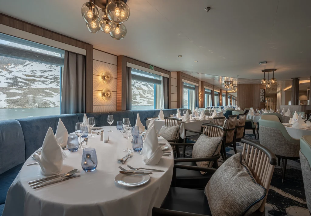 Set dining tables with white linen and blue velvet banquettes beside snow-covered mountain views