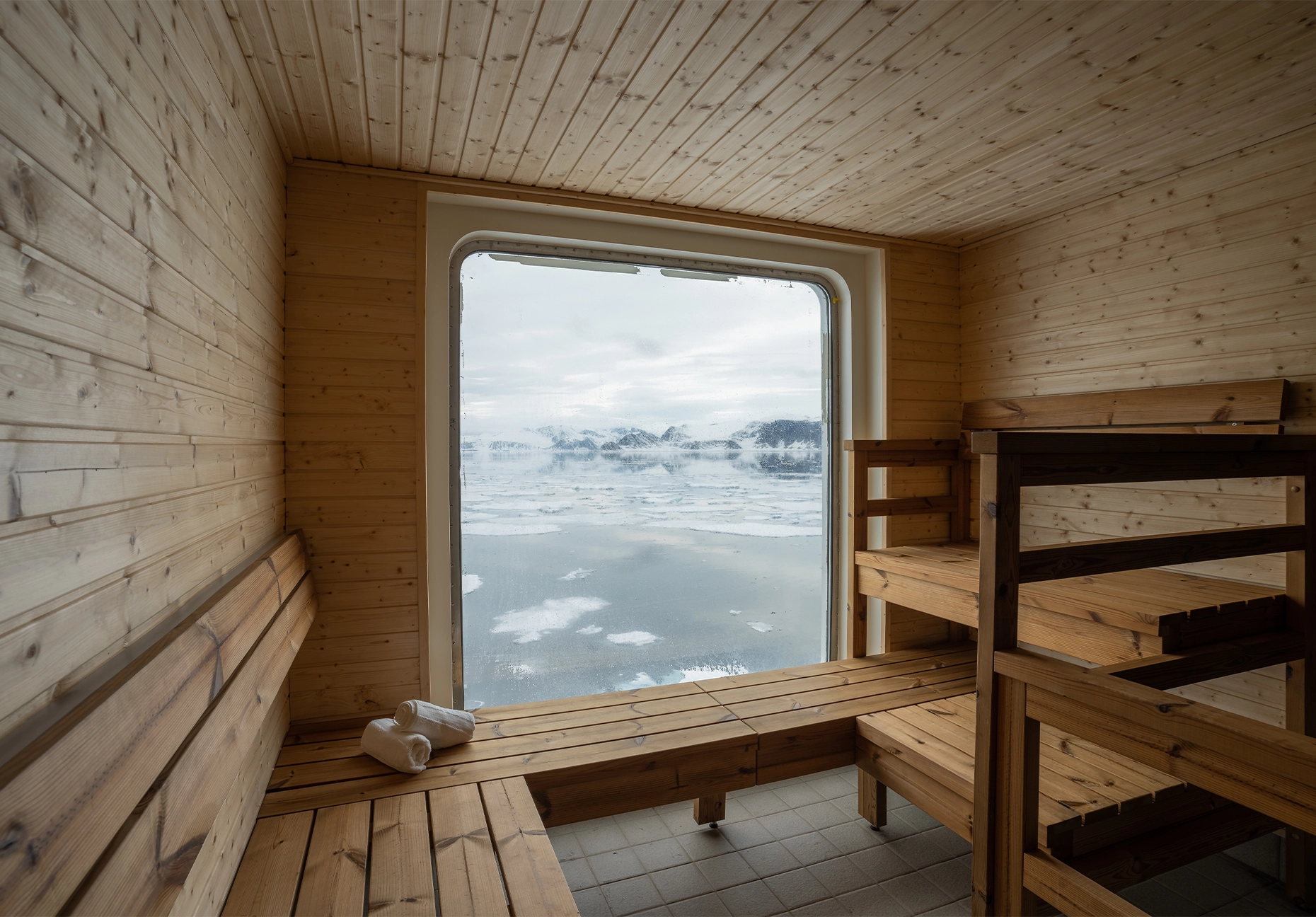 Pine-lined sauna with tiered benches facing a window overlooking drifting sea ice