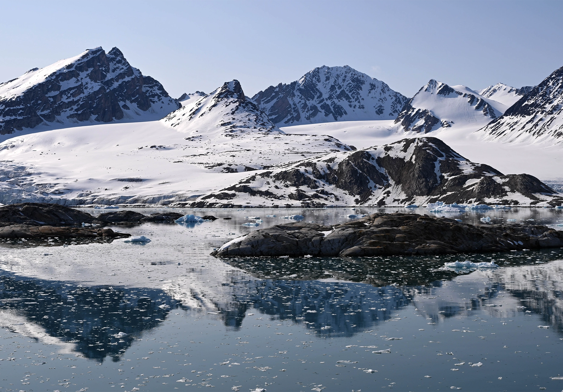 Rocky islets and drifting brash ice below a broad glacier and jagged white mountains