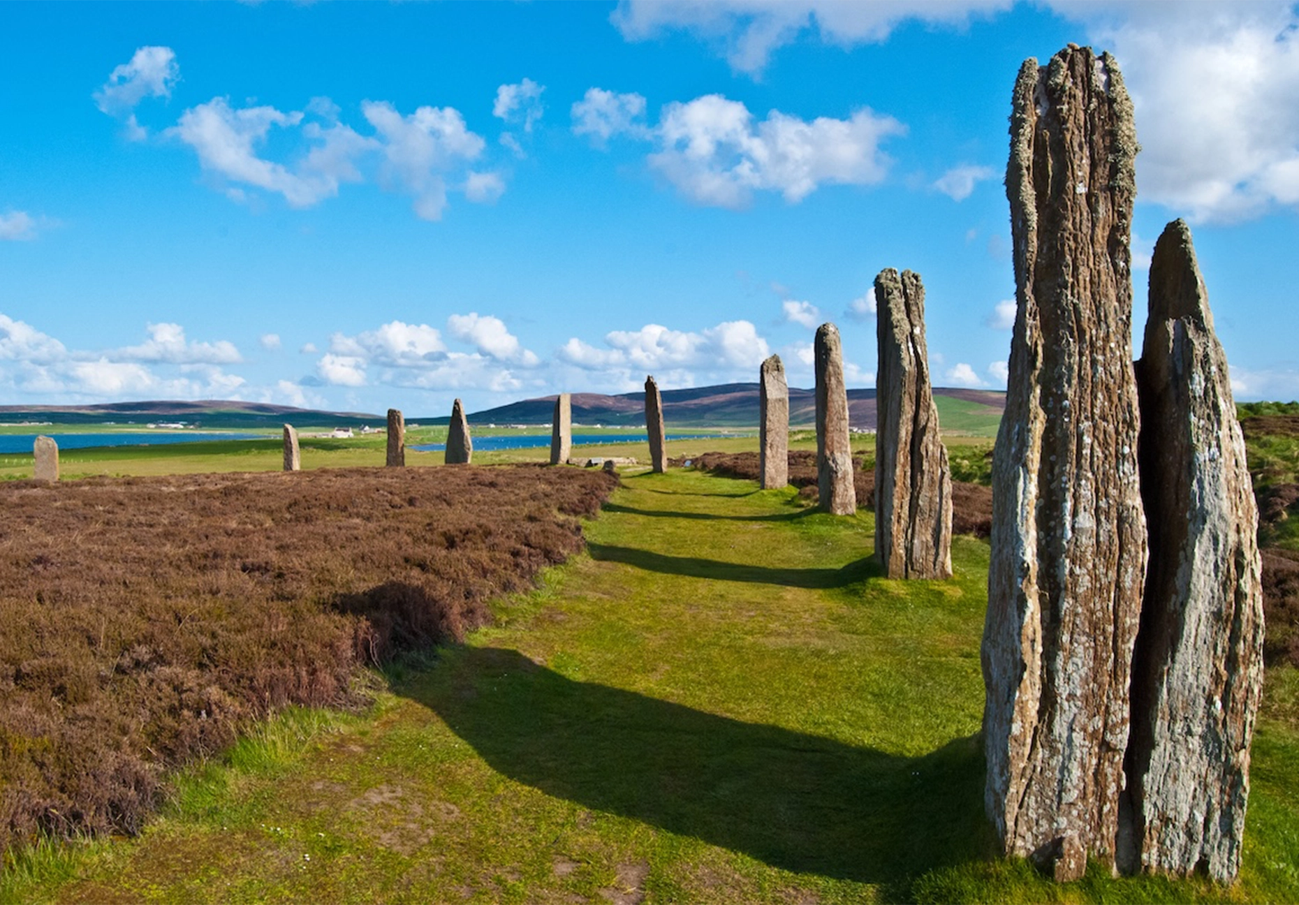 Weathered stone monoliths in a grassy circle with heather and a loch behind