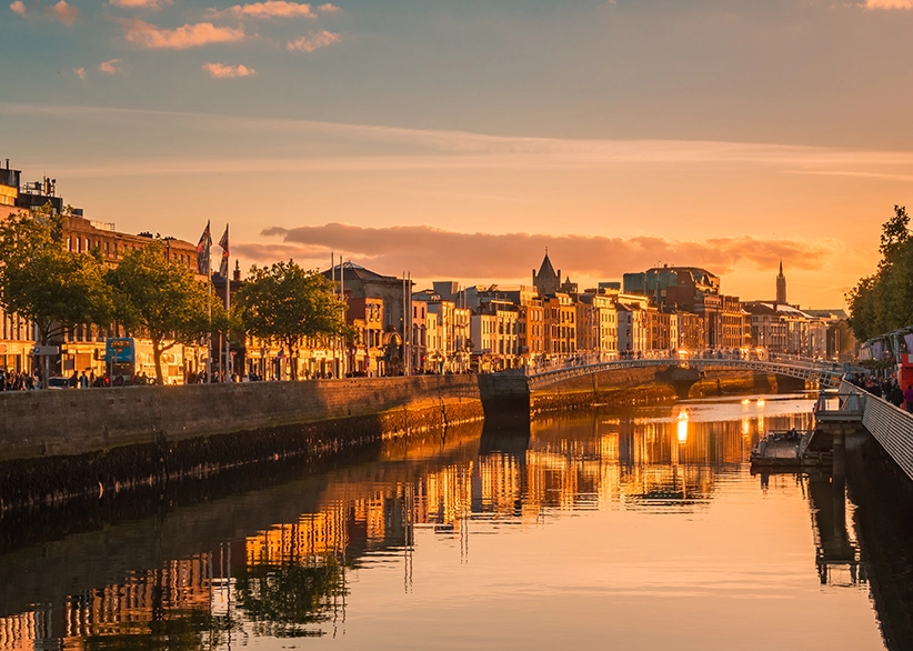 The Ha'penny Bridge and the River Liffey in Dublin at golden hour with warm light reflecting on the water and the city's quayside buildings glowing at sunset