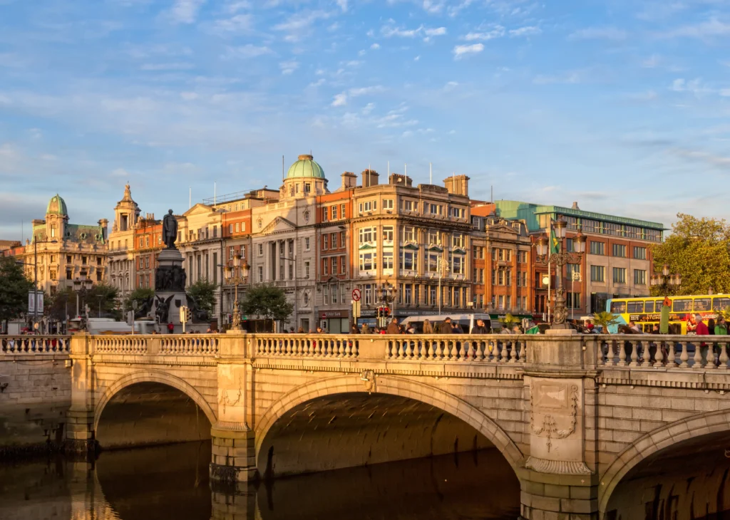 O'Connell Bridge over the River Liffey in Dublin, Ireland, bathed in golden light with historic buildings, the O'Connell Monument, and a yellow Dublin Bus in the background