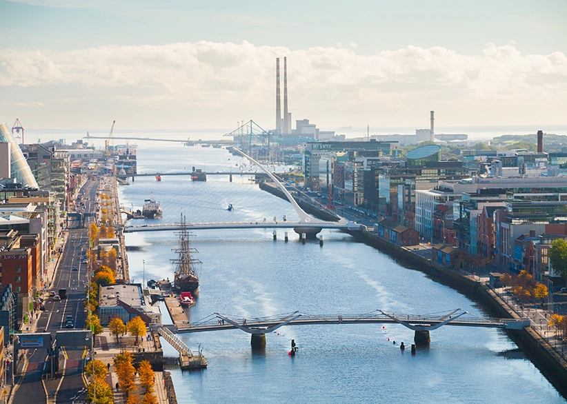 Aerial view of Dublin's Docklands looking east along the River Liffey with the Samuel Beckett Bridge, the Jeanie Johnston tall ship, and the Poolbeg chimneys in the distance