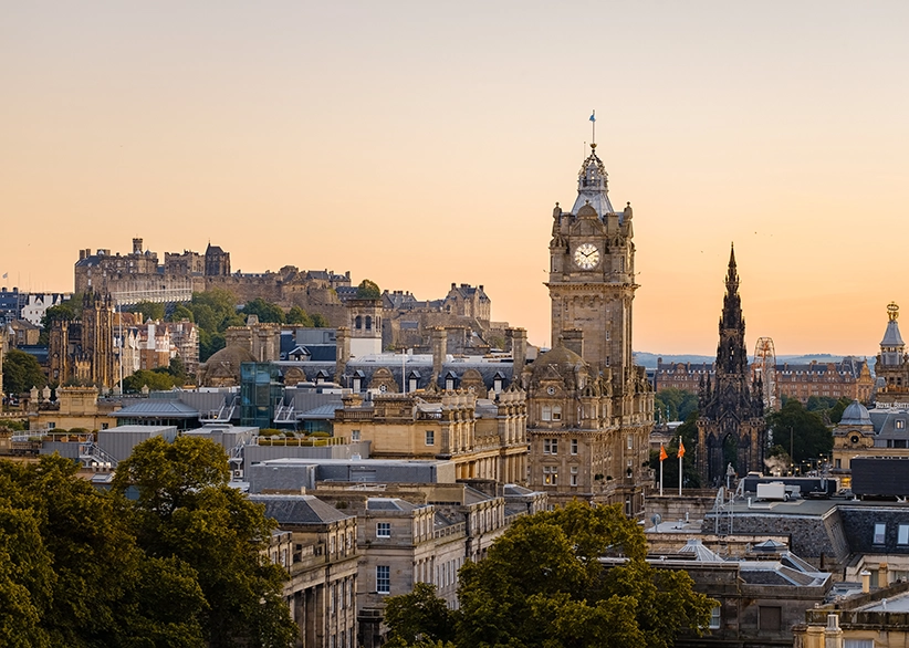 Edinburgh skyline at sunset with the Balmoral Hotel clock tower, the Scott Monument, and Edinburgh Castle on the hilltop in the background