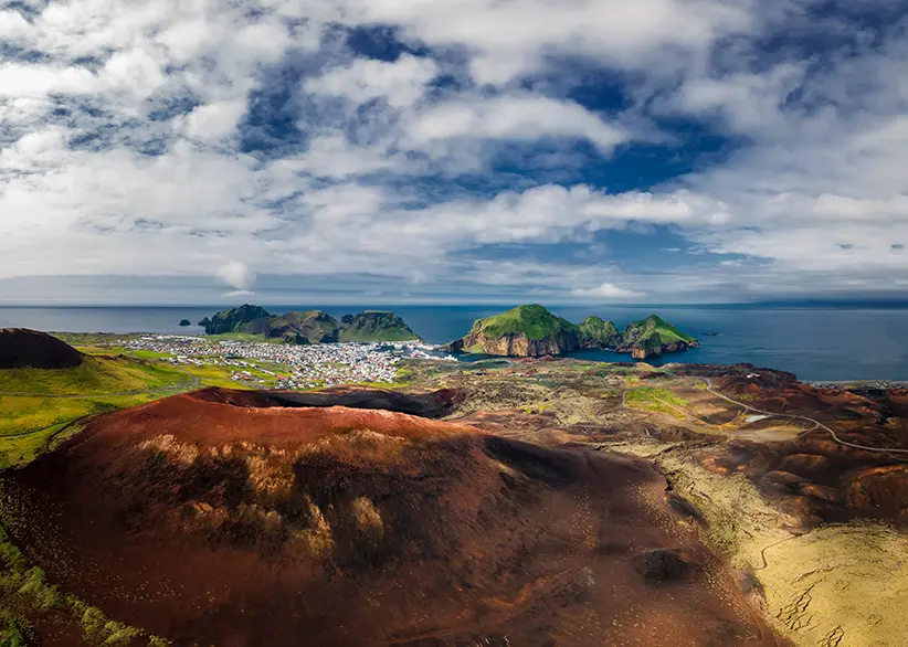 Aerial view from the red volcanic crater of Eldfell looking over the town of Heimaey, green cliffs, and the surrounding Atlantic Ocean on the Westman Islands, Iceland