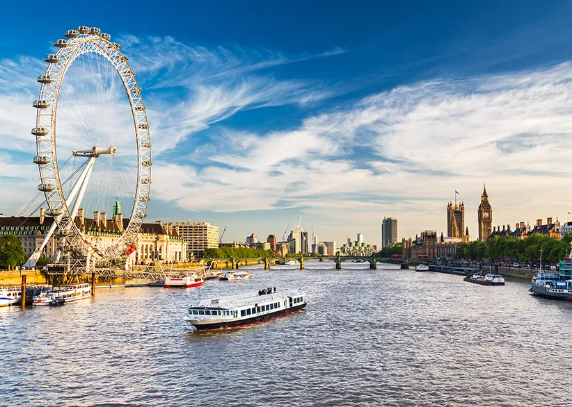 The London Eye on the South Bank of the River Thames with a river cruise boat, Westminster Bridge, and the Houses of Parliament with Big Ben in the background on a sunny day