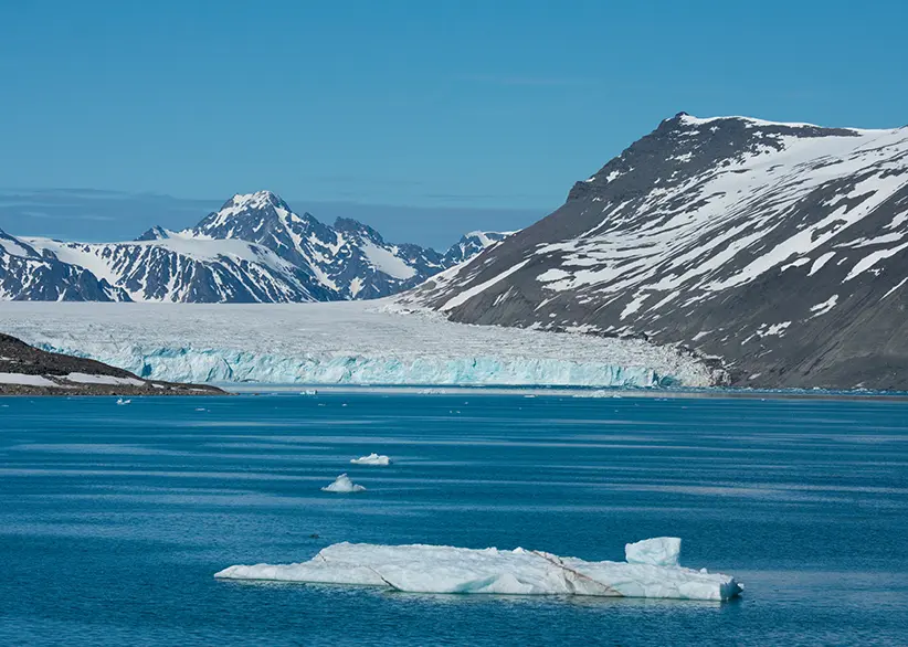 A blue tidewater glacier meeting the fjord with floating icebergs and snow-covered mountains in Northwest Spitsbergen National Park, Svalbard, Norway