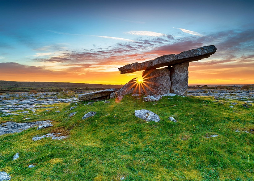Poulnabrone dolmen at sunset with a sunburst shining through the ancient stone portal tomb on the limestone karst landscape of the Burren, County Clare, Ireland