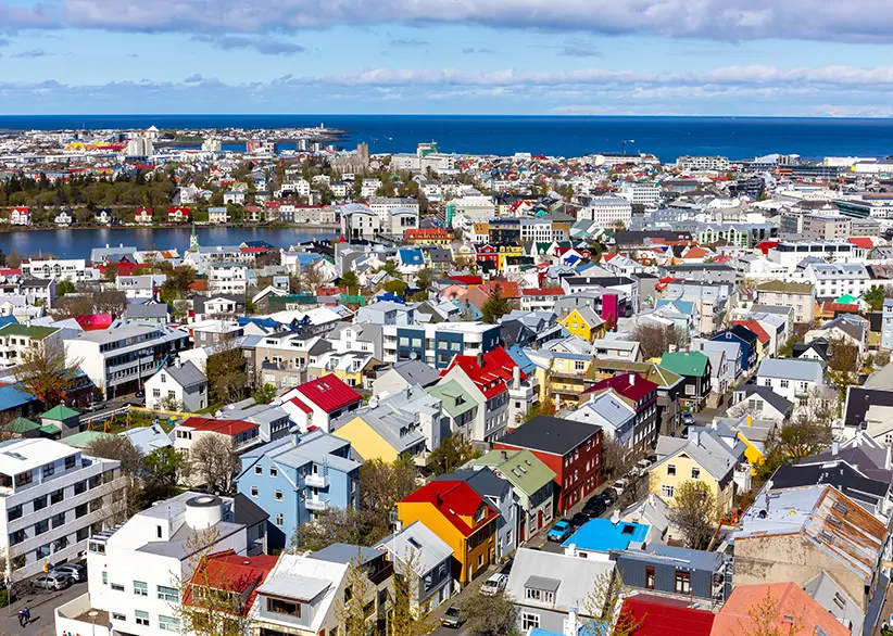 Aerial view of Reykjavik's colourful rooftops in red, yellow, blue, and green with Tjörnin lake and the Atlantic Ocean in the background on a sunny day