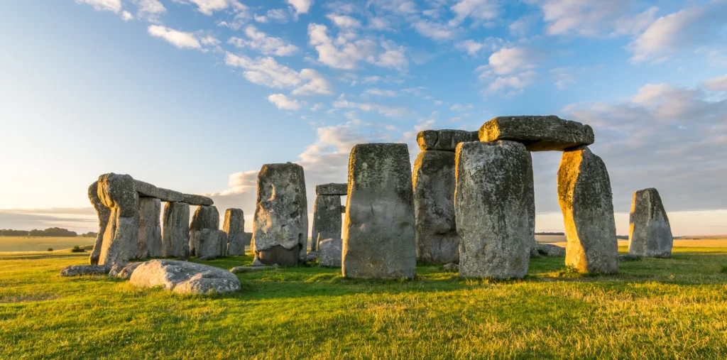Stonehenge's ancient standing stones and lintels on Salisbury Plain bathed in warm golden light under a blue sky with scattered clouds, Wiltshire, England