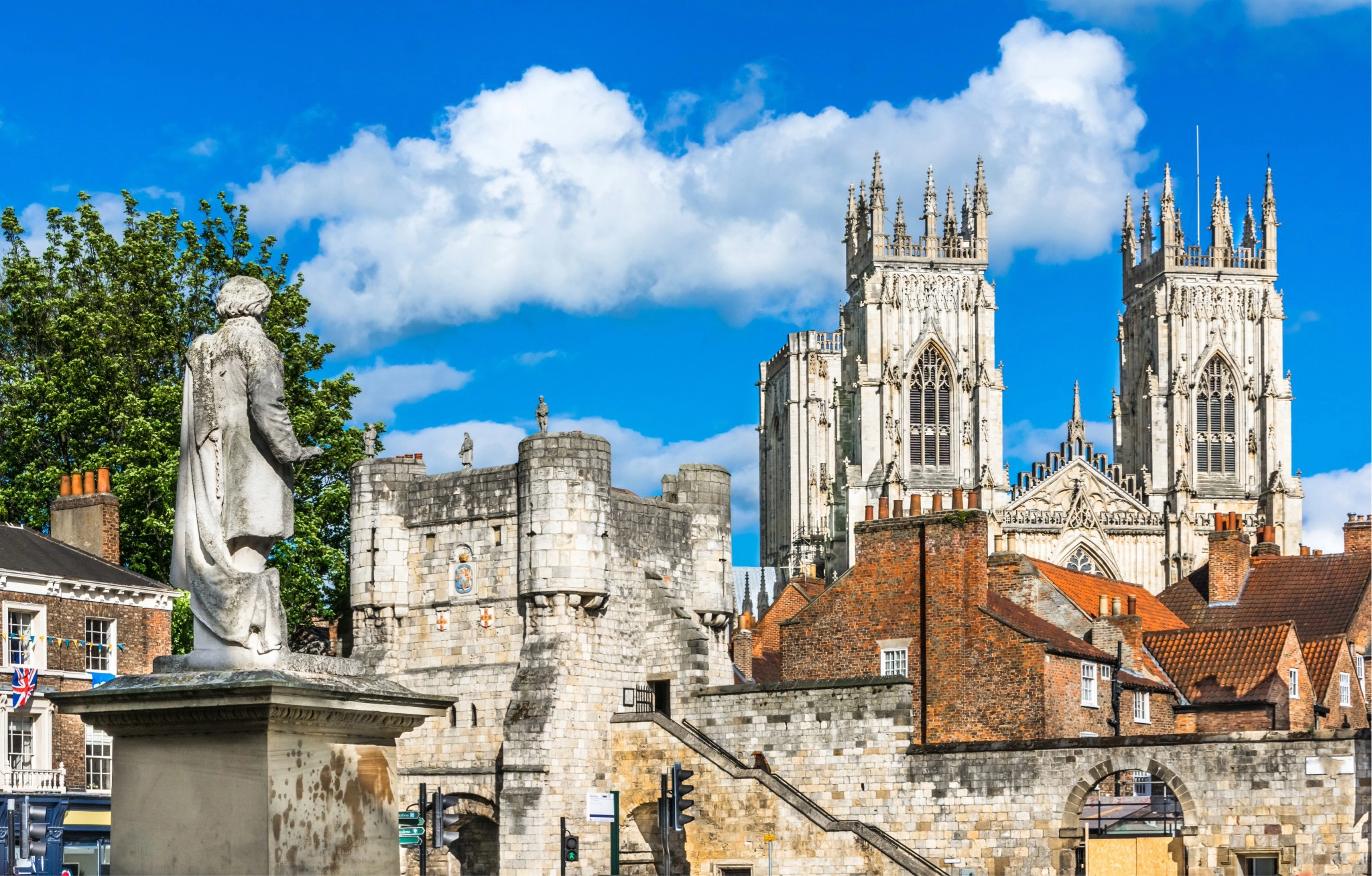View of York Minster's Gothic towers rising behind Bootham Bar's medieval city walls, with a statue in the foreground, York, England