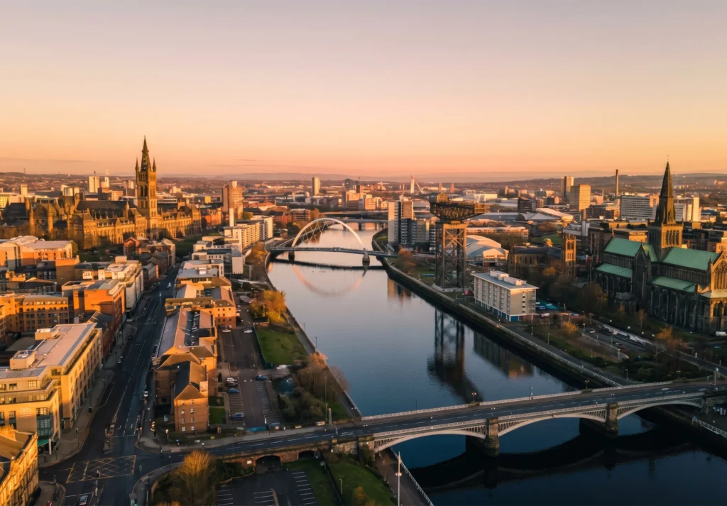 Golden sunset light over Glasgow's skyline, bridges, and the River Clyde seen from above.