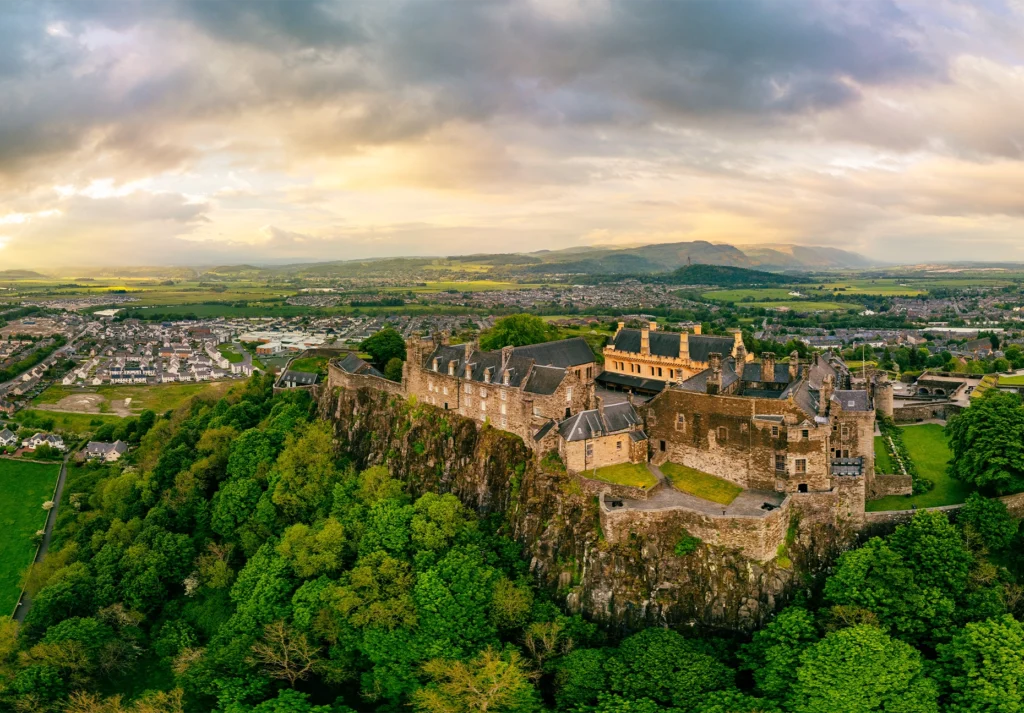 Stirling Castle sits atop a wooded crag above the town, with hills beyond at sunset.