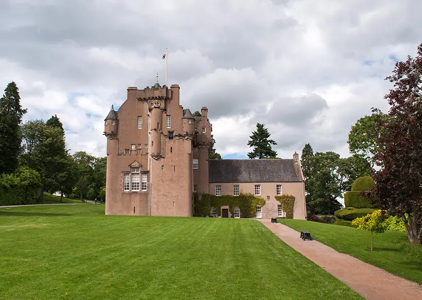 Crathes Castle's pink-harled tower house with turrets and manicured green lawns surrounded by mature trees and topiary near Braemar, Aberdeenshire, Scotland