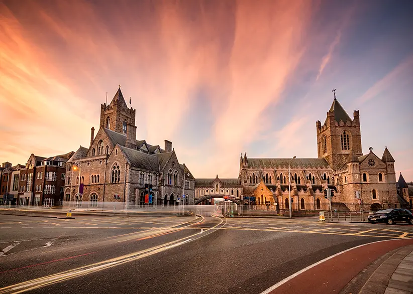 Christ Church Cathedral and Dublinia connected by their stone bridge at sunset with a dramatic pink and orange sky and light trails from passing traffic, Dublin, Ireland