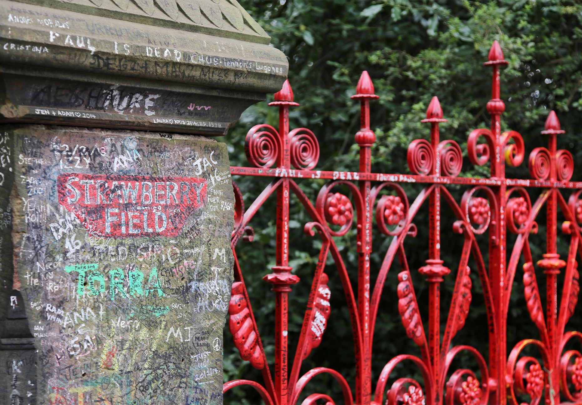 Fans' graffiti covers a stone gatepost beside the ornate red gates of Strawberry Field.