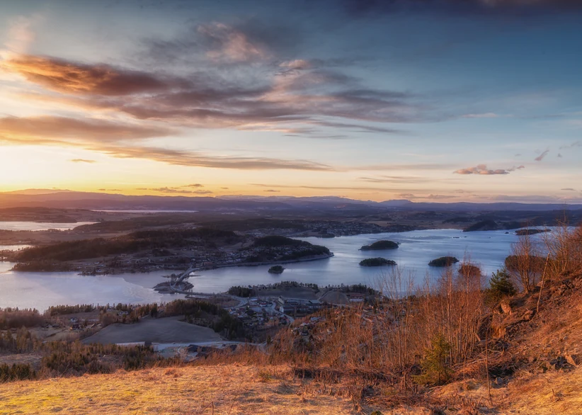 Aerial view at sunset of Lake Tyrifjord, with scattered small islands dotting the water, a lakeside town nestled among hills, and golden autumn foliage on the hillside in the foreground.