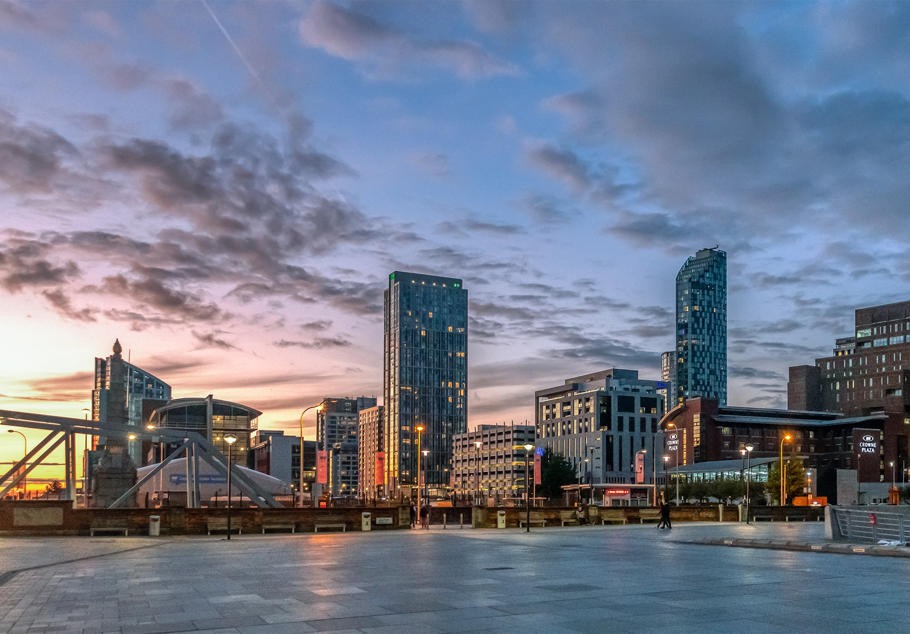 Modern high-rise towers and city buildings against a pink and blue dusk sky over an open plaza.