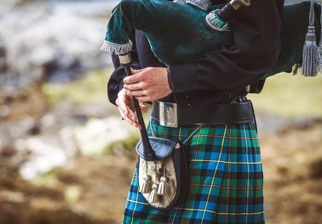 Close-up of a kilted piper in blue and green tartan playing bagpipes outdoors.