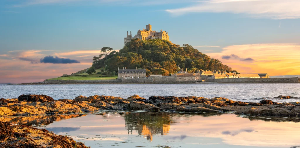 St Michael's Mount castle and harbour village on a tidal island in Mount's Bay at sunset with rocky foreshore, rock pools, and a colourful sky reflected in the water, Cornwall, England