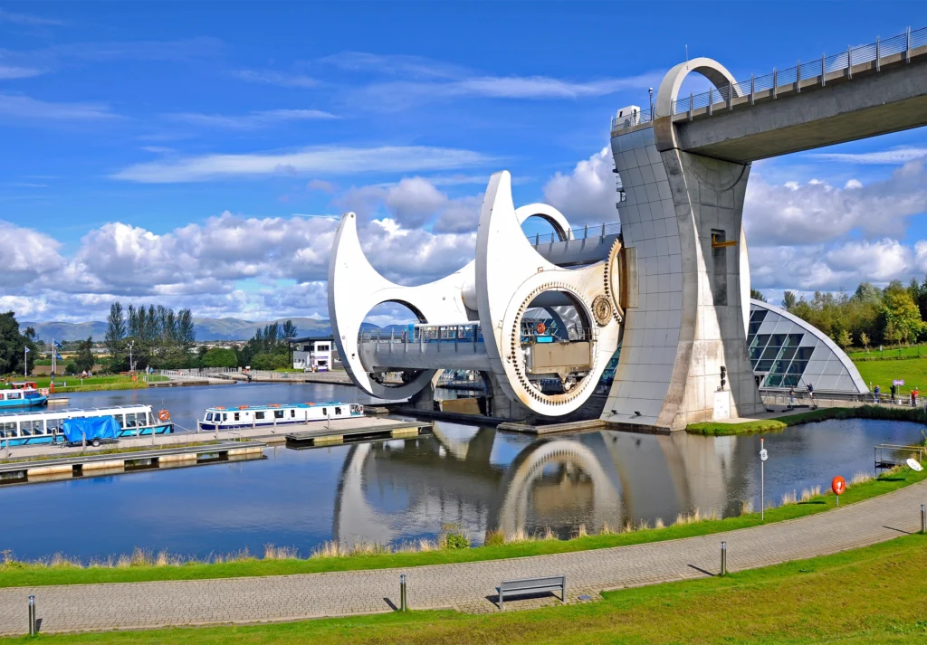 The Falkirk Wheel's white steel arms and aqueduct rise above canal boats moored below.