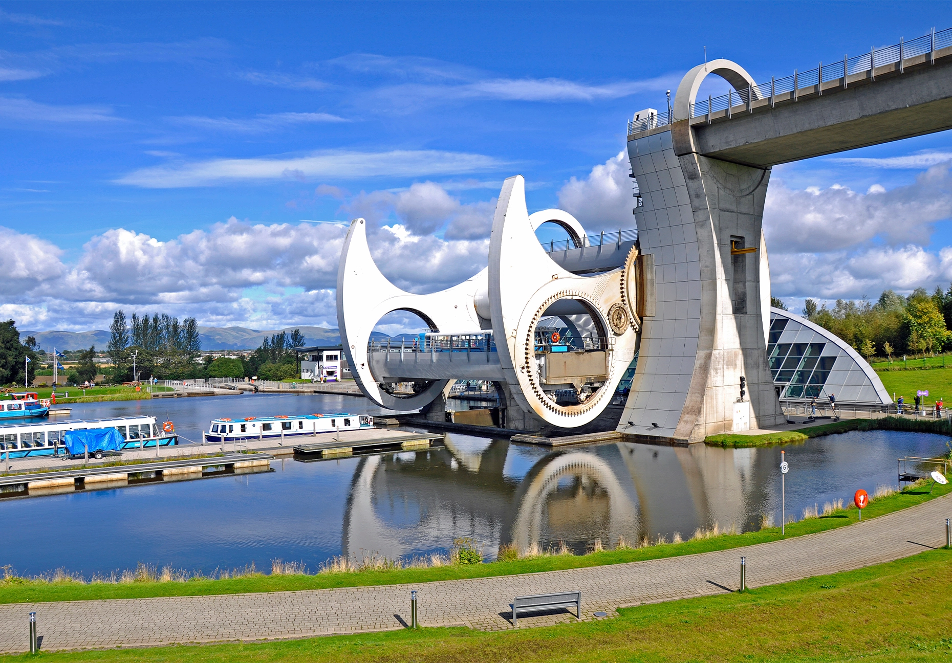 The Falkirk Wheel's white steel arms and aqueduct rise above canal boats moored below.