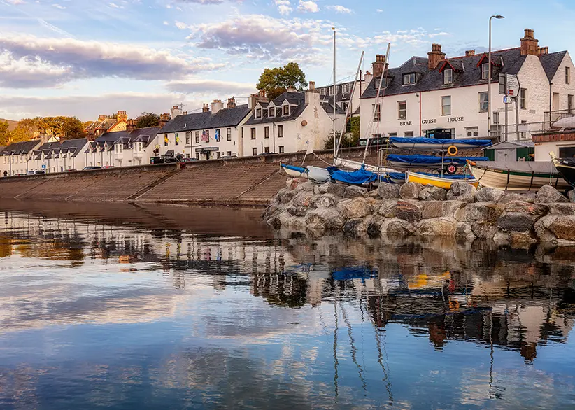The whitewashed waterfront buildings and small boats of Ullapool harbour reflected in calm water in the evening light, Scottish Highlands