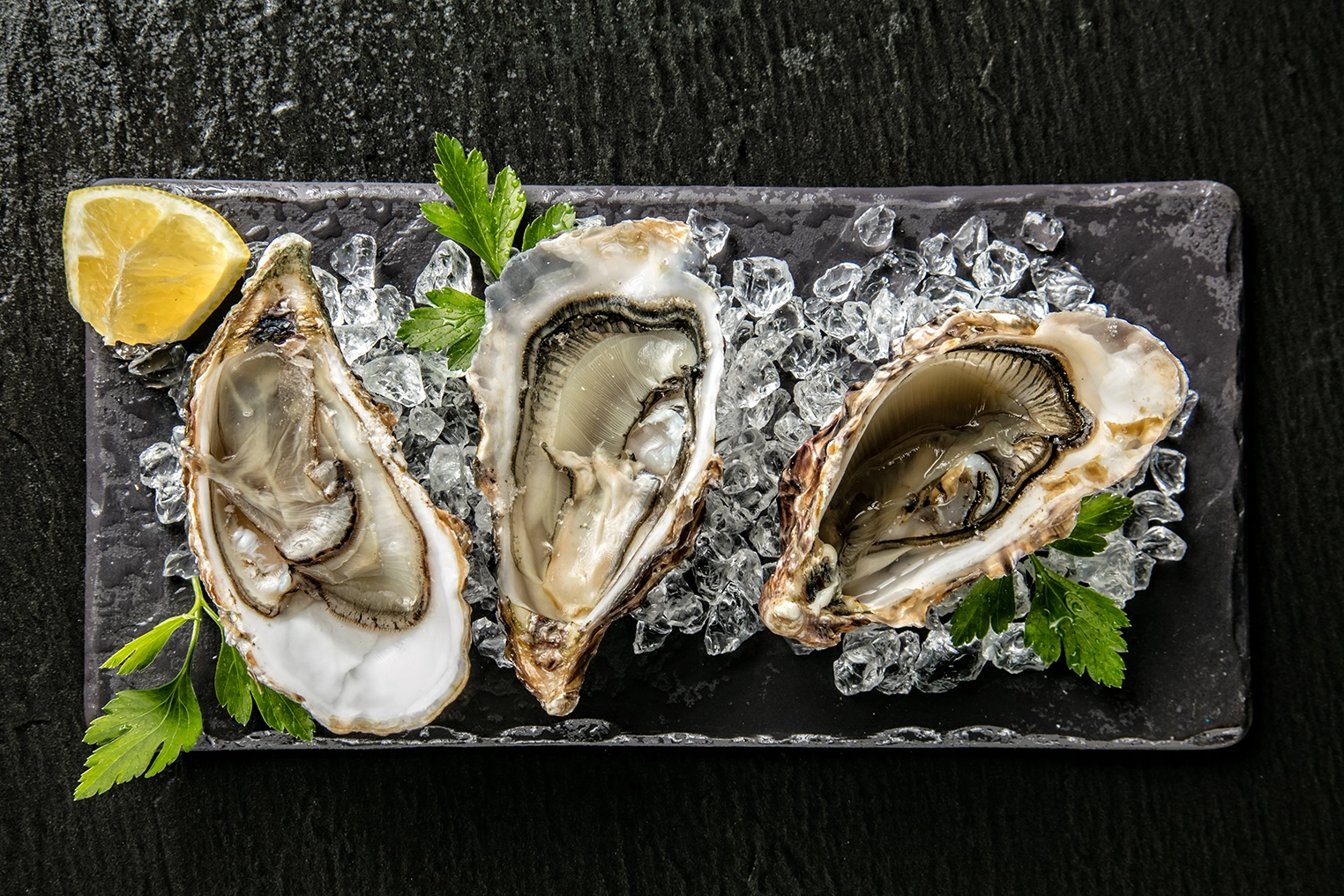 Three freshly shucked oysters rest on crushed ice with a lemon wedge and parsley.